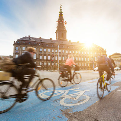 Blurred people going by bike in Copenhagen, with Christiansborg palace on background. Many persons prefer biking instead of taking car or bus to move around the city. Urban lifestyle concept.